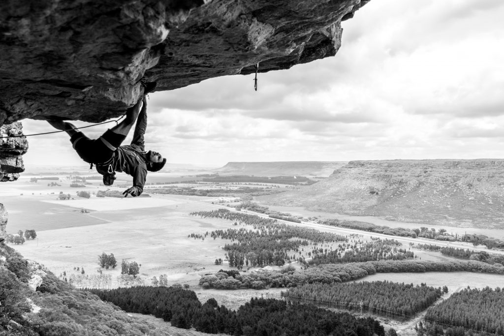 man climbing a boulder in black and white
